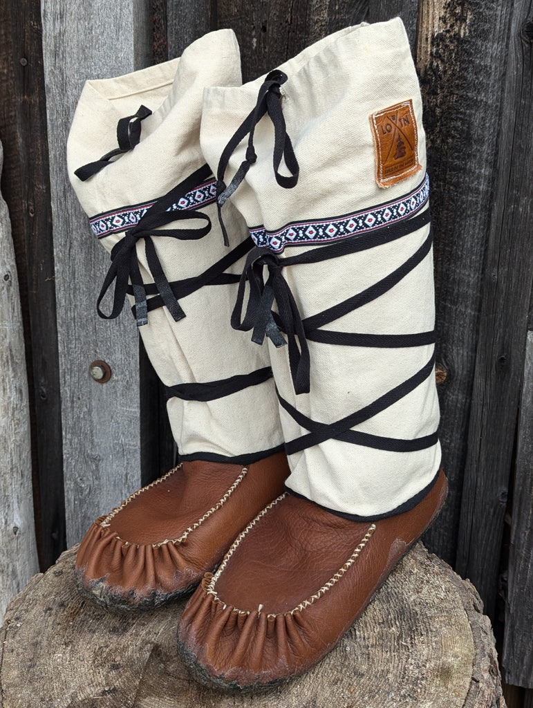 Pair of white and brown moccasin-style boots on a wooden stump with a rustic background.